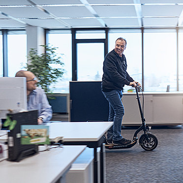 Mann, der mit E-Scooter durch Büroflur fährt