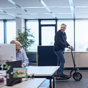 Mann fährt mit E-Scooter in Büroflur