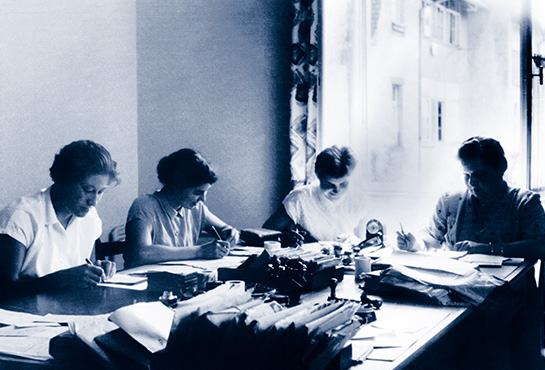 Altes schwarz-weiß Bild von vier Frauen, die auf Zetteln schreiben