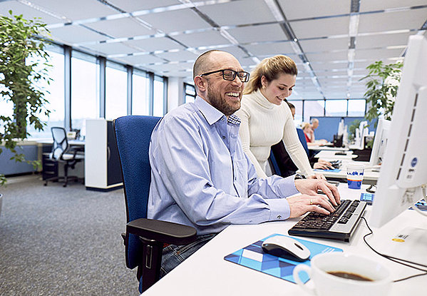 Mann, sitzend und Frau, stehend, arbeiten an einem Computer und lachen