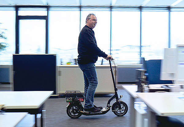 Mann, der mit E-Scooter durch Büroflur fährt