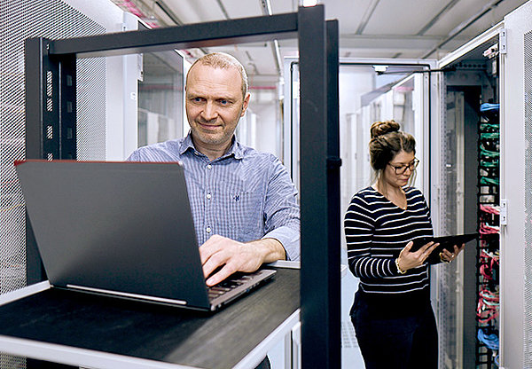 Mann mit Laptop und Frau mit Tablet in einem Server Raum