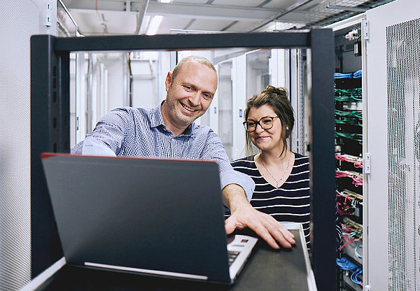 Mann und Frau schauen zusammen auf einen Laptop in einem Server Raum