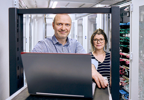 Mann und Frau, die in einem Server Raum auf einen Laptop schauen