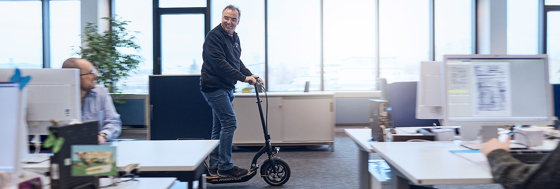 Mann, der mit E-Scooter durch Büroflur fährt