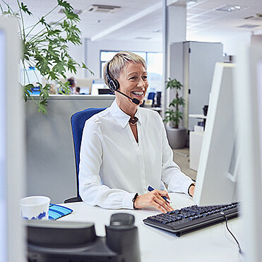 Lachende Frau mit Headset vor Computer sitzend