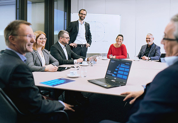 Besprechung von sieben Mitarbeitern an großem Tisch