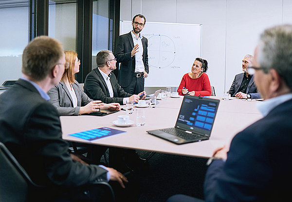 Besprechung von sieben Mitarbeitern an großem Tisch