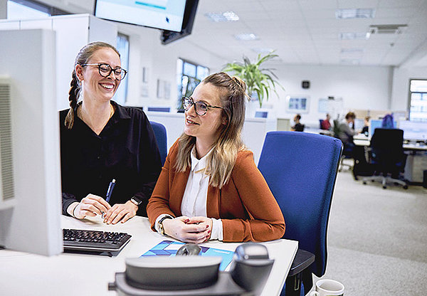 Zwei Frauen sitzen an einem Computer und lachen