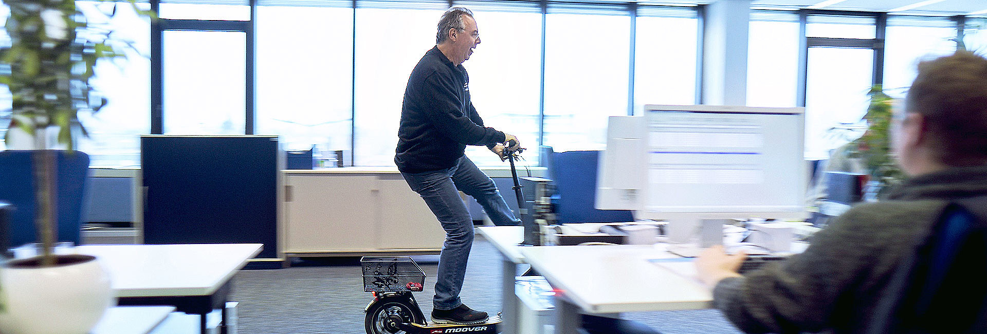 Mann fährt mit E-Scooter durch ein Büro