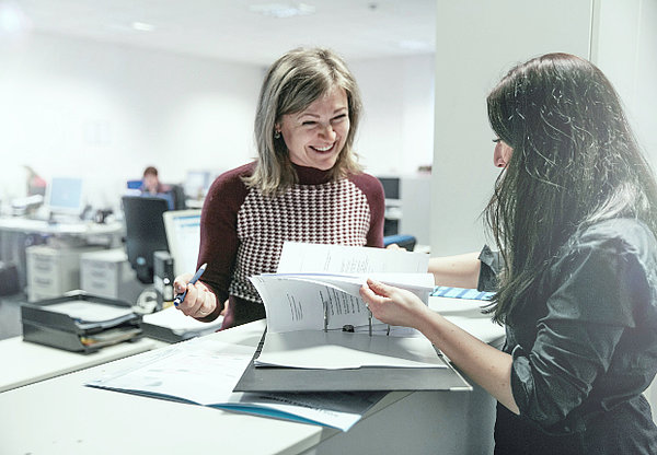 Zwei Frauen schauen in einen Ordner und lachen