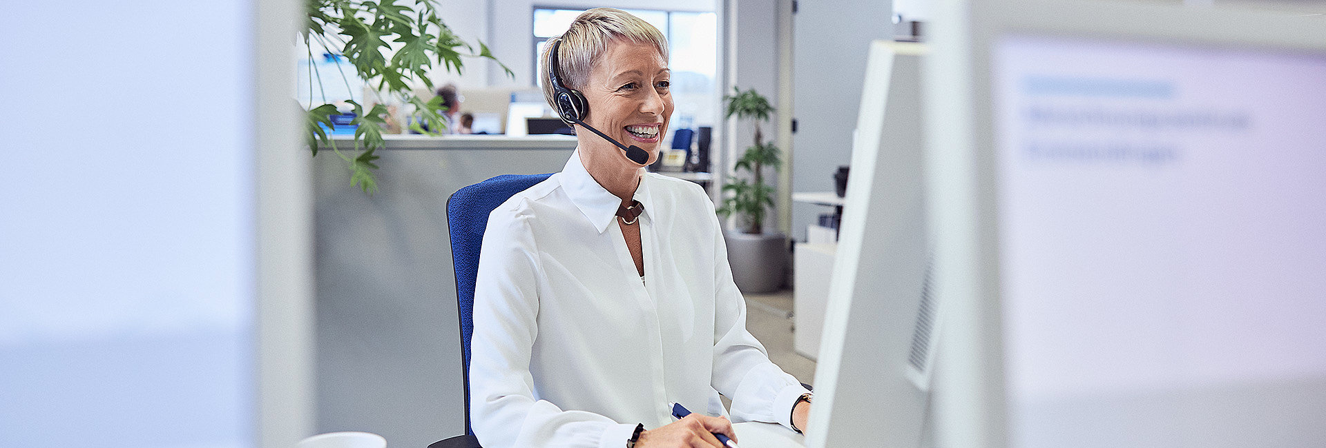 Telefonierende Frau mit Headset hinter Bildschirmen